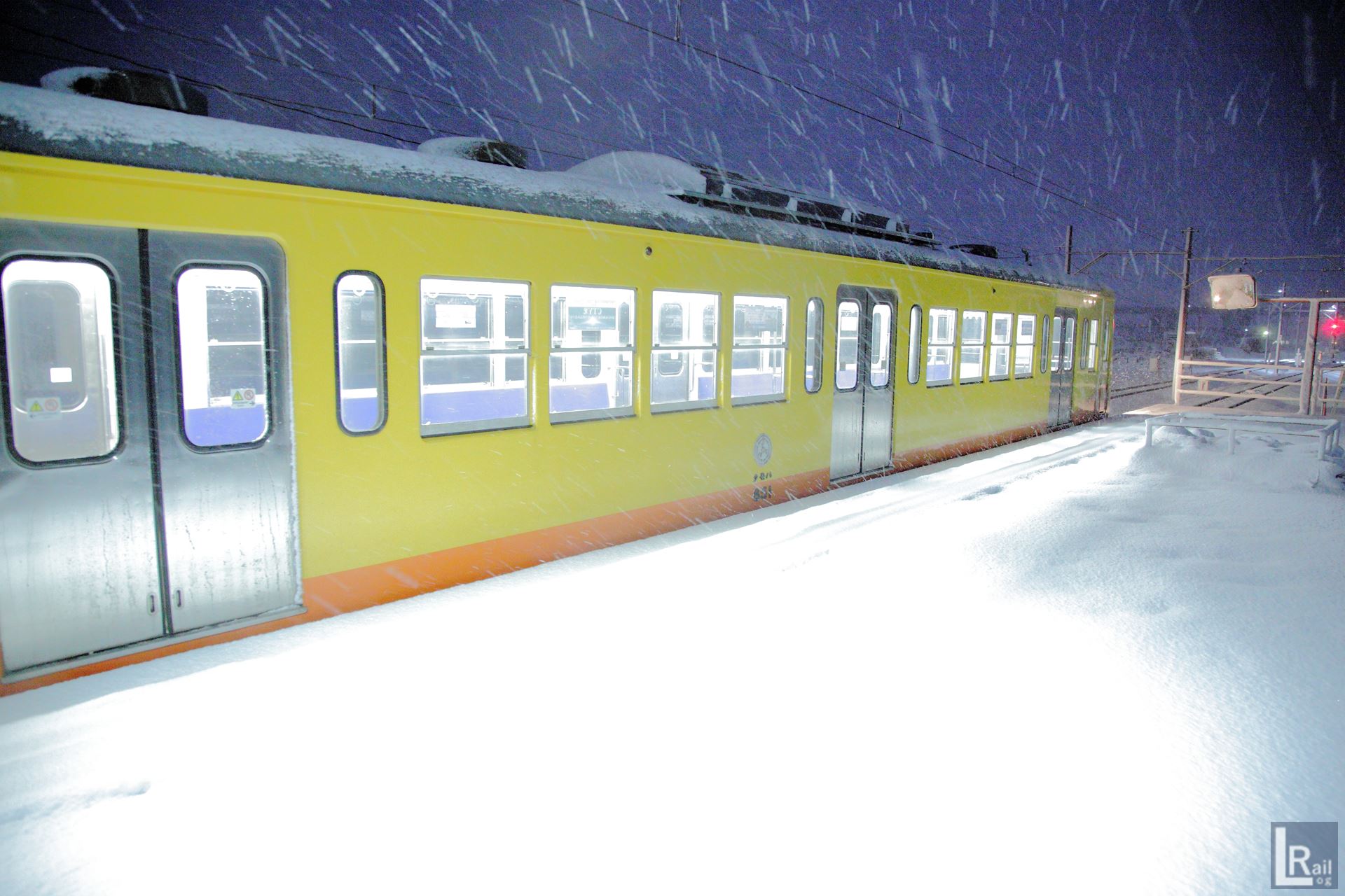 電車の明かりが雪の積もったホームを照らす